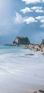 Serene beach view with rocky island and soft blue skies.