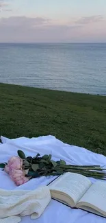 Serene coastal picnic setup with ocean view, book, and pink flowers.