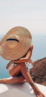 Woman in hat sits by tranquil ocean view.