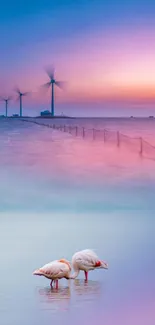 Serene sunrise over ocean with wind turbines and flamingos.