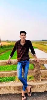 Man leaning on a rustic bridge over a rural landscape.