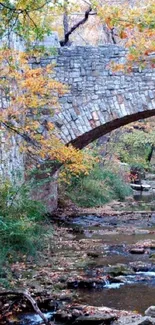 Scenic stone bridge over a serene creek in autumn foliage.