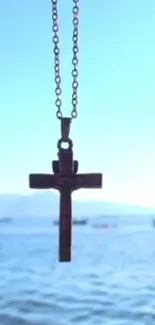 Wooden cross pendant over calm water with clear blue sky.