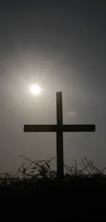 Silhouette of a cross with a sunrise background on a mobile wallpaper.