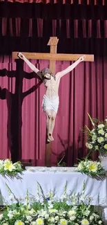 Serene crucifix with floral arrangement and burgundy drapes.