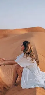 Woman in white dress sitting on sand dunes.