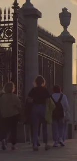 People walking by ornate gates at sunset in the city.