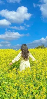 Person standing in a yellow flower field under a bright blue sky.