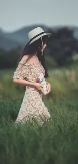 Woman in floral dress walking through green field with mountains in background.