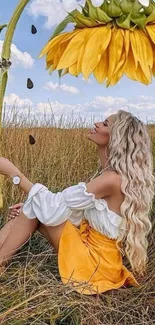 Woman sitting in field under a large sunflower with blue skies.