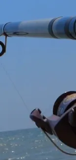 Fishing rod extended over a calm ocean under a clear blue sky.