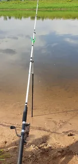 Fishing rod beside a calm river under a clear sky.