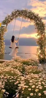 A woman in white on a floral swing at sunset by the ocean.