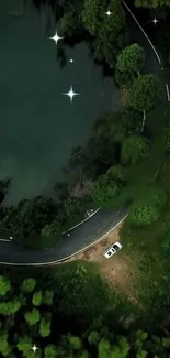 A serene aerial view of a winding forest road with a car by a tranquil lake.