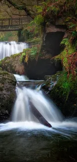 Serene waterfall flowing through lush green forest with wooden bridge.