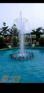 A serene park fountain with blue water and surrounding greenery.