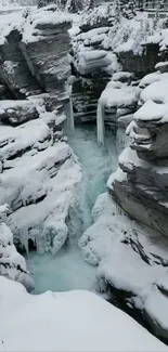 Snow-covered rocky gorge with icy waterfall in winter landscape.