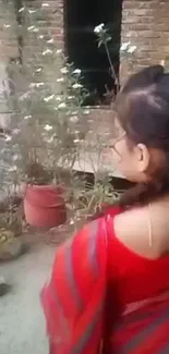 Woman in red saree admires garden flowers.