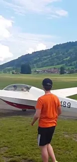 Glider plane at rest in lush green mountain landscape under a blue sky.