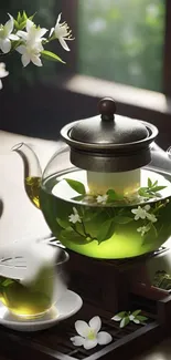 Glass teapot with green tea and jasmine flowers by a window.