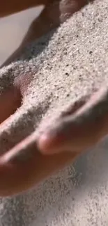 Mobile wallpaper showing a hand allowing sand to flow gently through fingers.