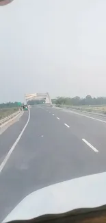 Tranquil highway with bridge and greenery under a vast sky.