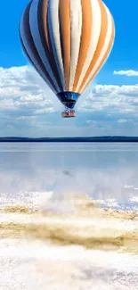 Hot air balloon floating under a blue sky reflected in a tranquil lake.