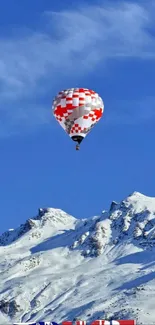 Hot air balloon over snowy mountains under blue sky.