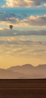 Hot air balloon over desert with mountains and clouds in a serene landscape.