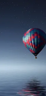 Hot air balloon floats above calm waters with a starlit night backdrop.