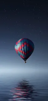 Hot air balloon reflecting over a calm night sea under starry sky.