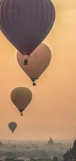 Hot air balloons float above misty landscape at sunrise.