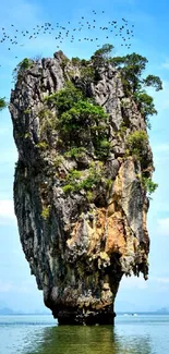 Towering island cliff with birds and blue sky.