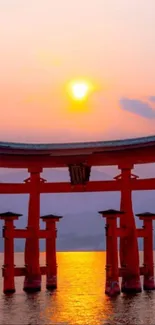 Japanese sunset with torii gate and orange sky over water.