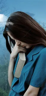 Woman in blue dress holding book in forested background.