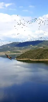 A serene lake with a bird flock flying over mountains and clear blue sky.