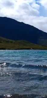 Serene mountain lake under blue sky with hills in the background.