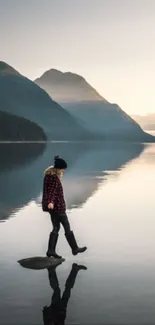 Person reflected on a calm lake with mountains in the background.