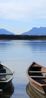 Two rowboats on a tranquil lake with mountains and blue sky.