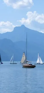 Sailboats float on a tranquil lake with mountains and clouds in the background.