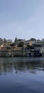 View of a serene city by the lake with reflections under a clear blue sky.