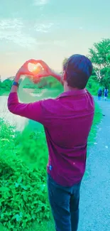 Man making heart shape at sunset by a lake.