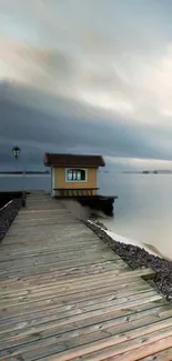 A peaceful lakeside view with a wooden house and cloudy sky.