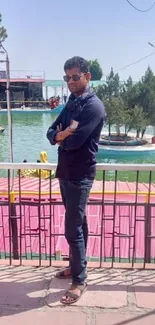 Man standing by a lake in a park with green trees and calm waters.