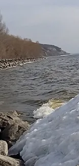 Serene lakeside view with icy and rocky shore under a clear sky.