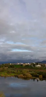 Tranquil countryside and lake under a cloudy sky.