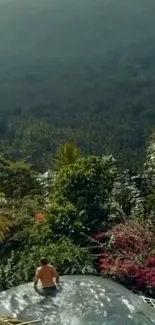 Man sitting by an infinity pool with lush green landscape.