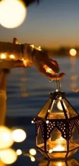 A hand holding lantern over water with glowing lights in dark blue night.