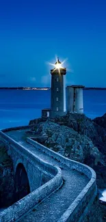Lighthouse against a deep blue evening sky on rocky coastline.