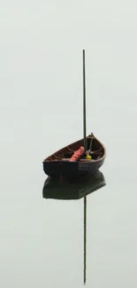 A lone wooden boat reflecting on calm, light gray water.